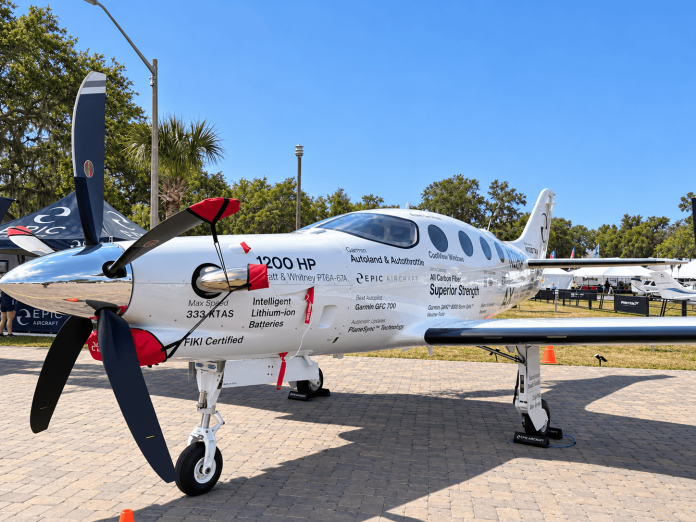 Epic E1000 AX Autoland-equipped turboprop on display in sunshine, showing its five-blade propeller, cockpit windows and white fuselage.